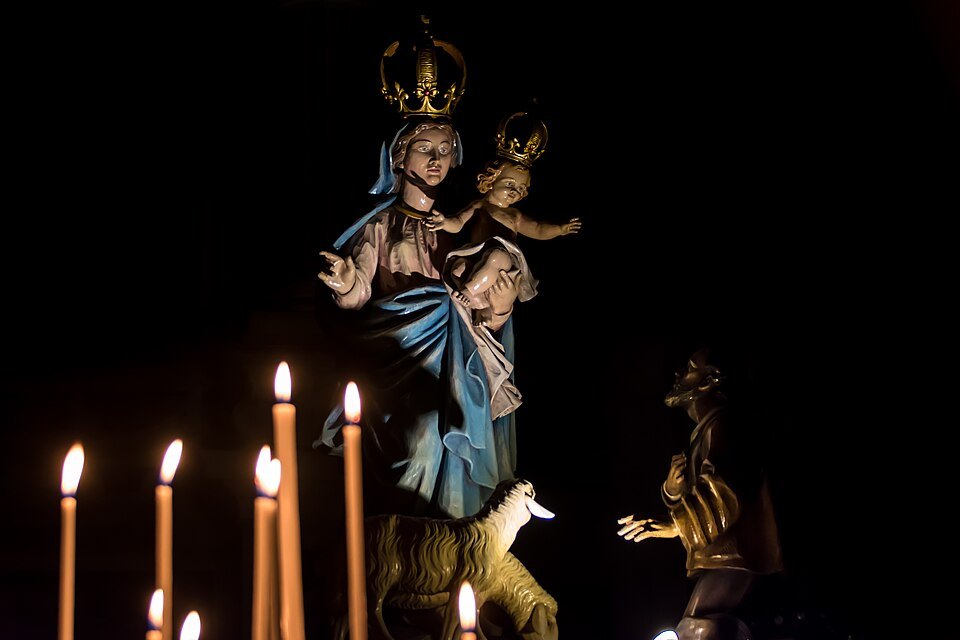 A carved Madonna carried in procession, lit by candles in the Annunziata