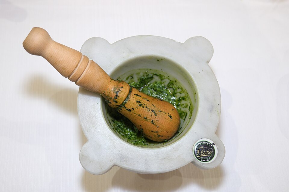 Pesto being pounded in a marble mortar with a wooden pestle