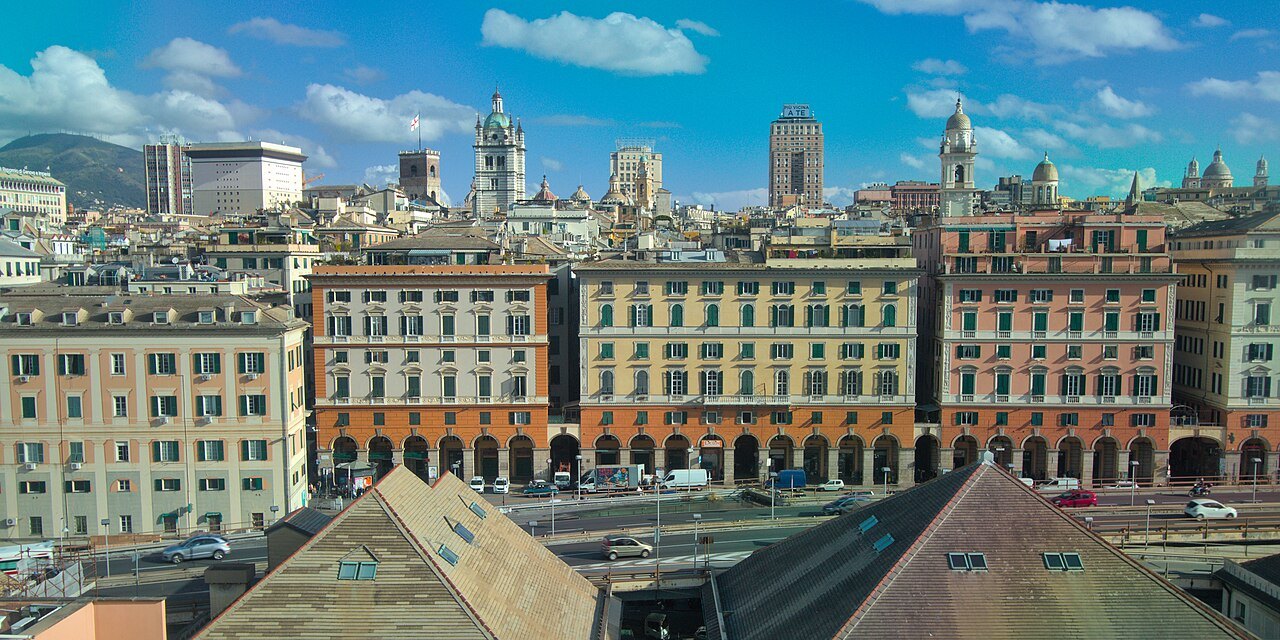 The long painted facades of Piazza Caricamento and the old town rising behind them, seen from the Bigo