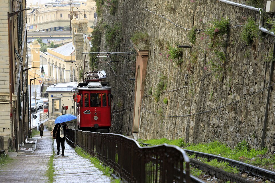 A red rack-railway car climbing the Principe–Granarolo line in the rain